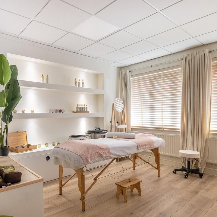 De massagetafel met roze plaid tussen de planten en de verlichte wandplanken in de behandelruimte Nature